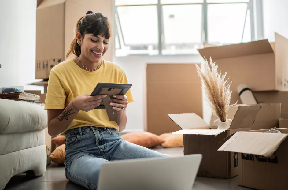 Woman smiles while holding a photo and unpacking boxes in her new home. 