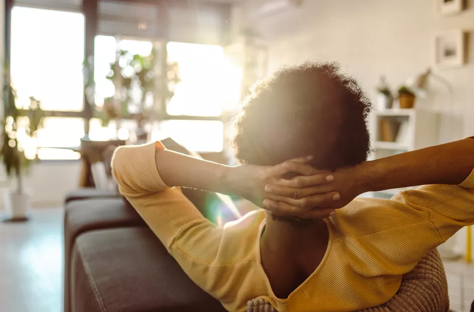 A woman relaxes on the couch as sun peaks through a window.