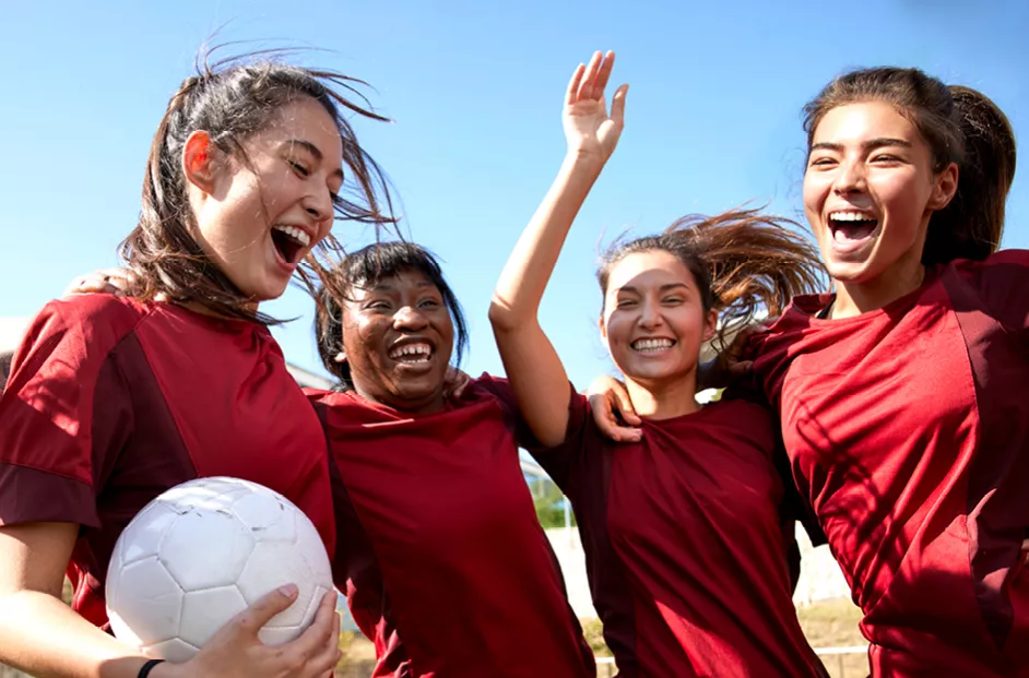 Group of four young female soccer players celebrate.