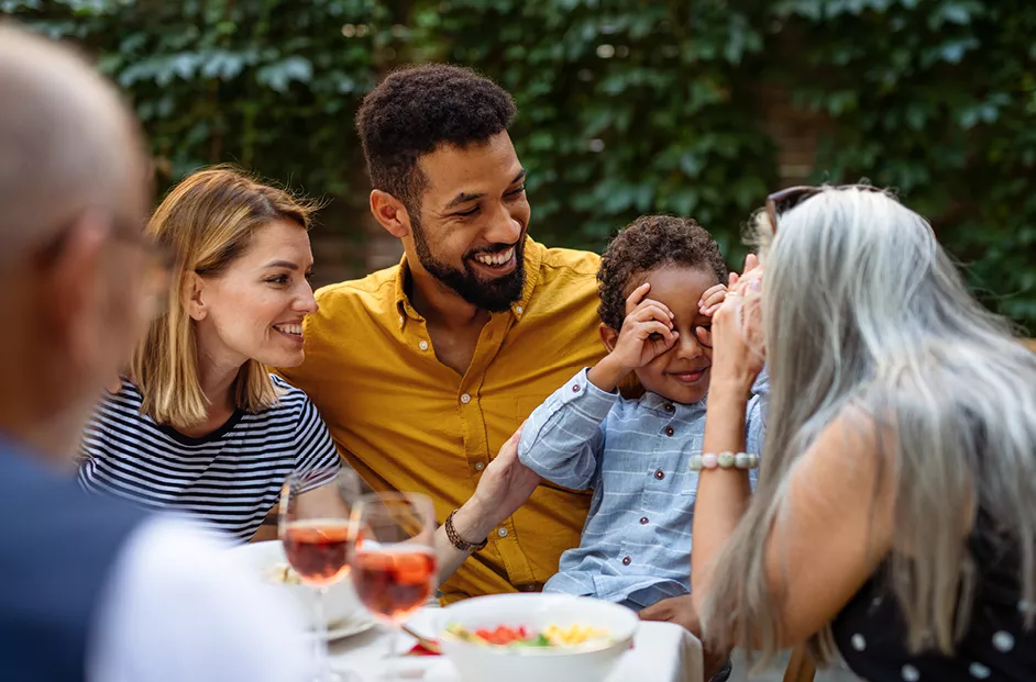 A happy family celebrates at a table with food and drinks. Two family members are making faces at one another.