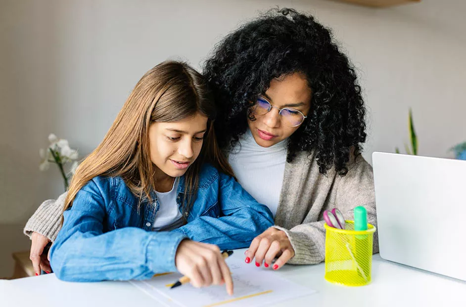 A woman helping a young girl with her homework.