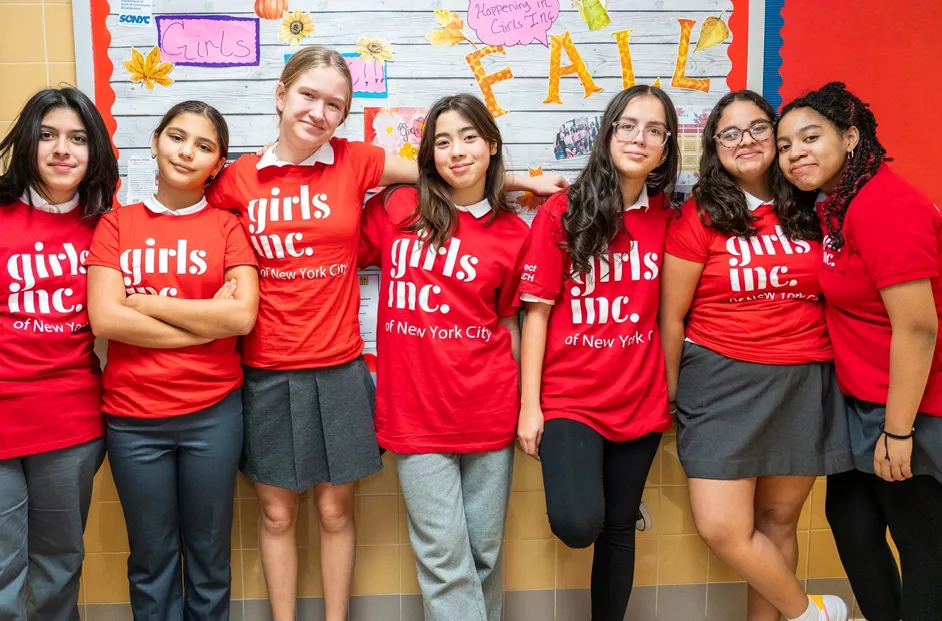 Group of girls pose outside of a classroom in red Girls Inc. t-shirts.