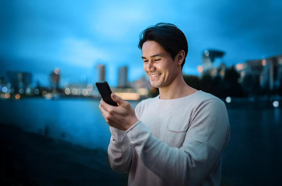 Image of a man looking at his phone with the backdrop of a city against a river in the background.