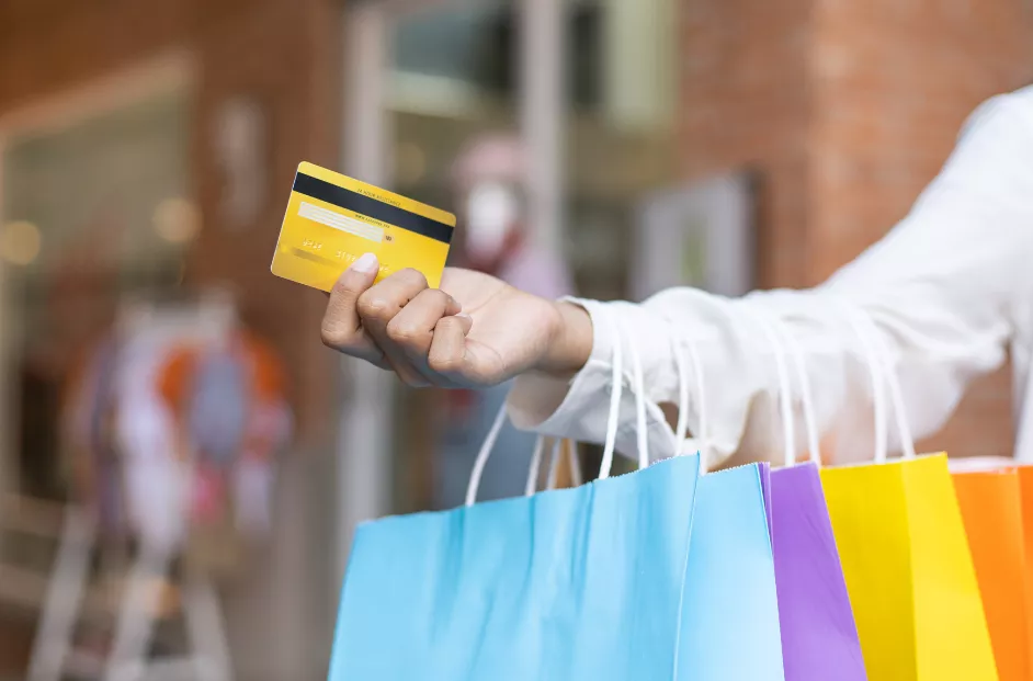 Stock image with an extended arm and hand holding a credit card and four shopping bags.