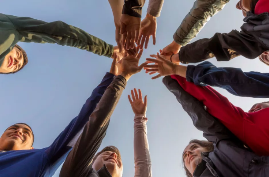 Group of students standing in circle with their hands overlapping in a celebratory fashion.