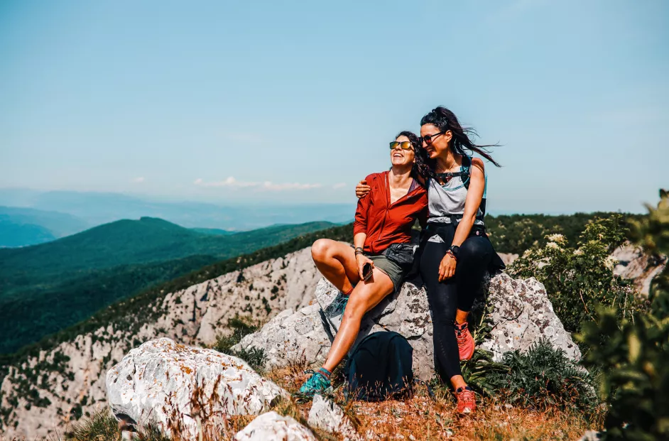 Two females smile at the top of a mountain range.