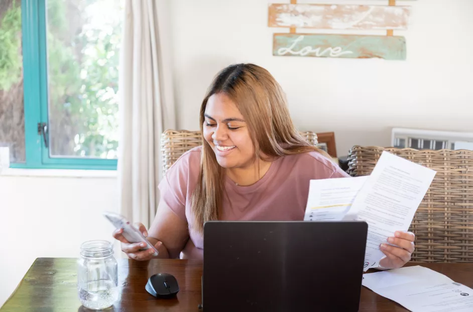 Female smiles while holding papers and viewing her smart phone and laptop.