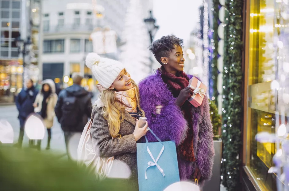 Two females dressed in winter clothing stare at a holiday shopping window display.