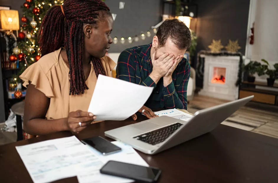 A couple appears stressed while reviewing bills. Holiday background.