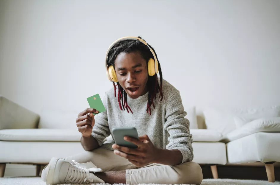 Shocked young man using smart phone with credit card at home 