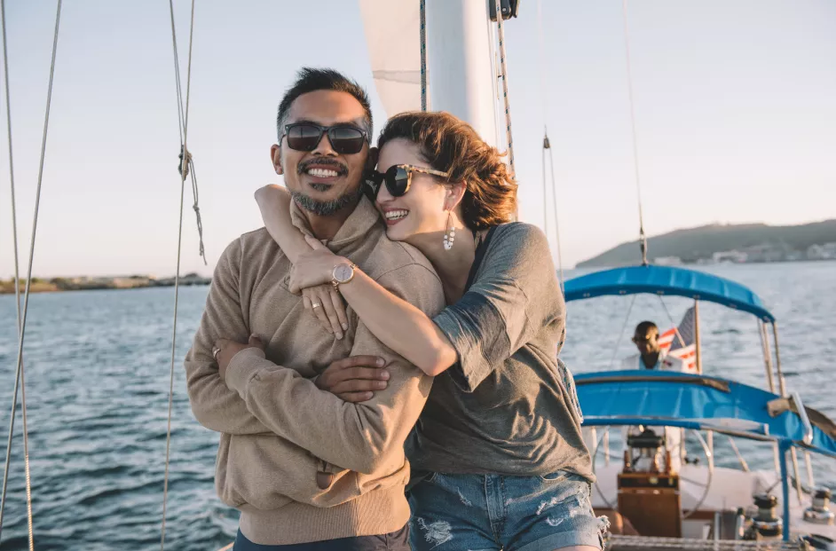 Photo of a couple on a yacht. The woman has her arms around her partner.