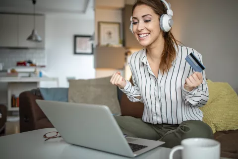 Woman wearing headphones celebrates while she makes an online purchase.
