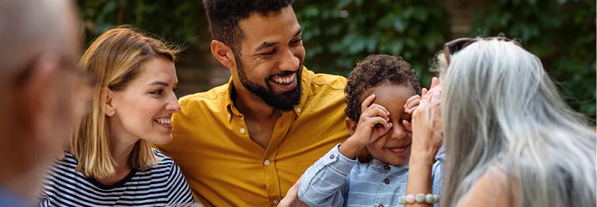 A happy family celebrates at a table with food and drinks. Two family members are making faces at one another.
