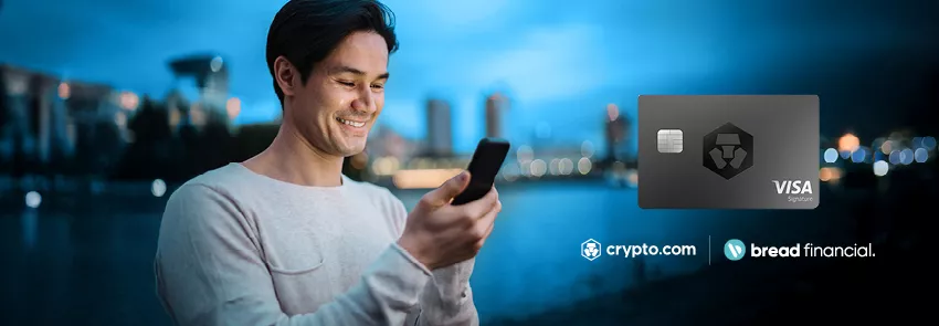 Man looks at phone with the backdrop of a city against the water included in the background. Logo lockup featuring the Crypto.com and Bread Financial logos is featured in the lower right corner.