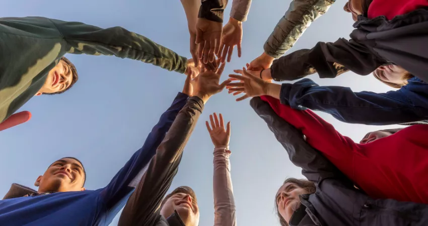 Group of students standing in circle with their hands overlapping in a celebratory fashion.