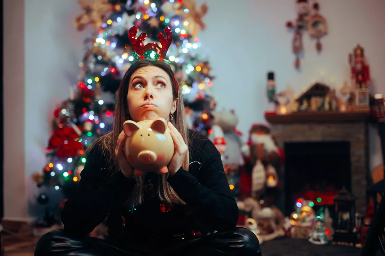 Stressed young woman holding a piggy bank and regretting holiday spendings