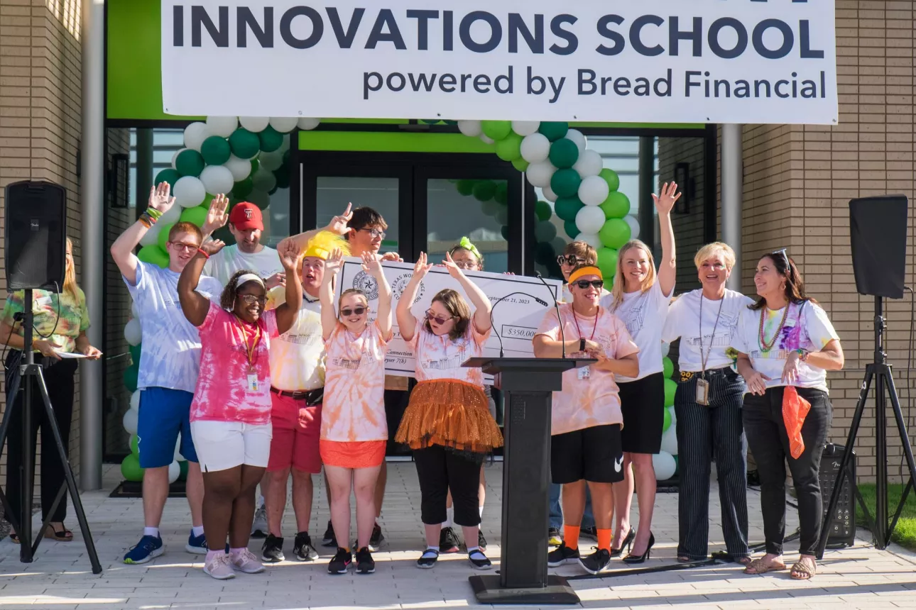 Group celebrates building opening behind a lectern. Photo includes a banner that reads "Innovations School powered by Bread Financial."